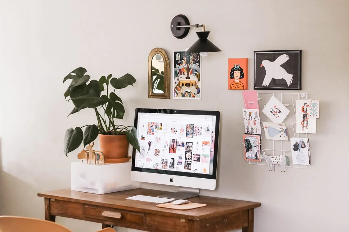 Aufgeräumter Schreibtisch mit Computer, Pflanze und Notizen an der Wand
